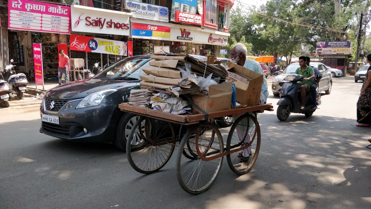 A kabadiwala pushing a cart stacked with cardboard and newspapers through a busy Bhopal street